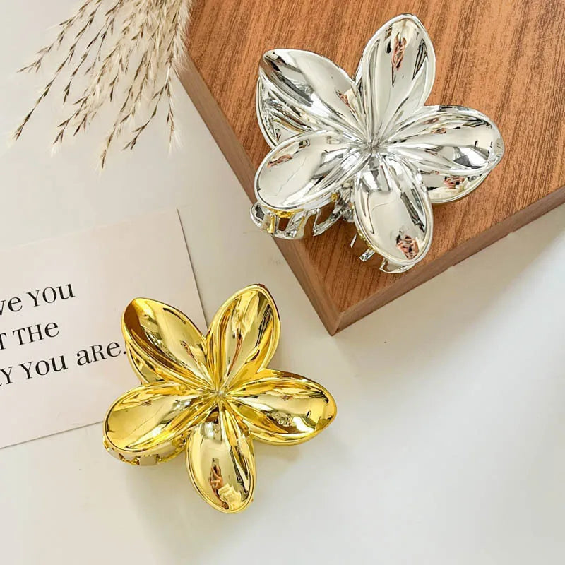 Hawaiian gradient flower hair claw clips with silver and gold flower shapes on a wood tray