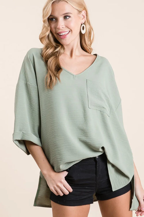 Sage green flowy woven V-neck top with chest pocket and rolled-up cuffs