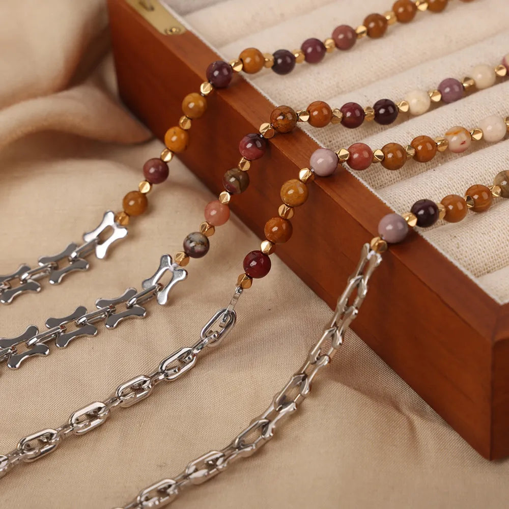 Beaded necklace with multicolor round stones and silver-tone chain draped across a wooden box