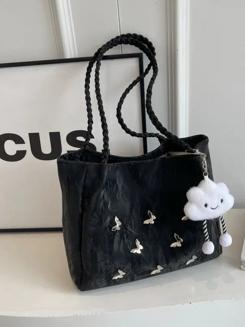 Black tote bag with butterfly pattern, braided handles, and a white plush charm