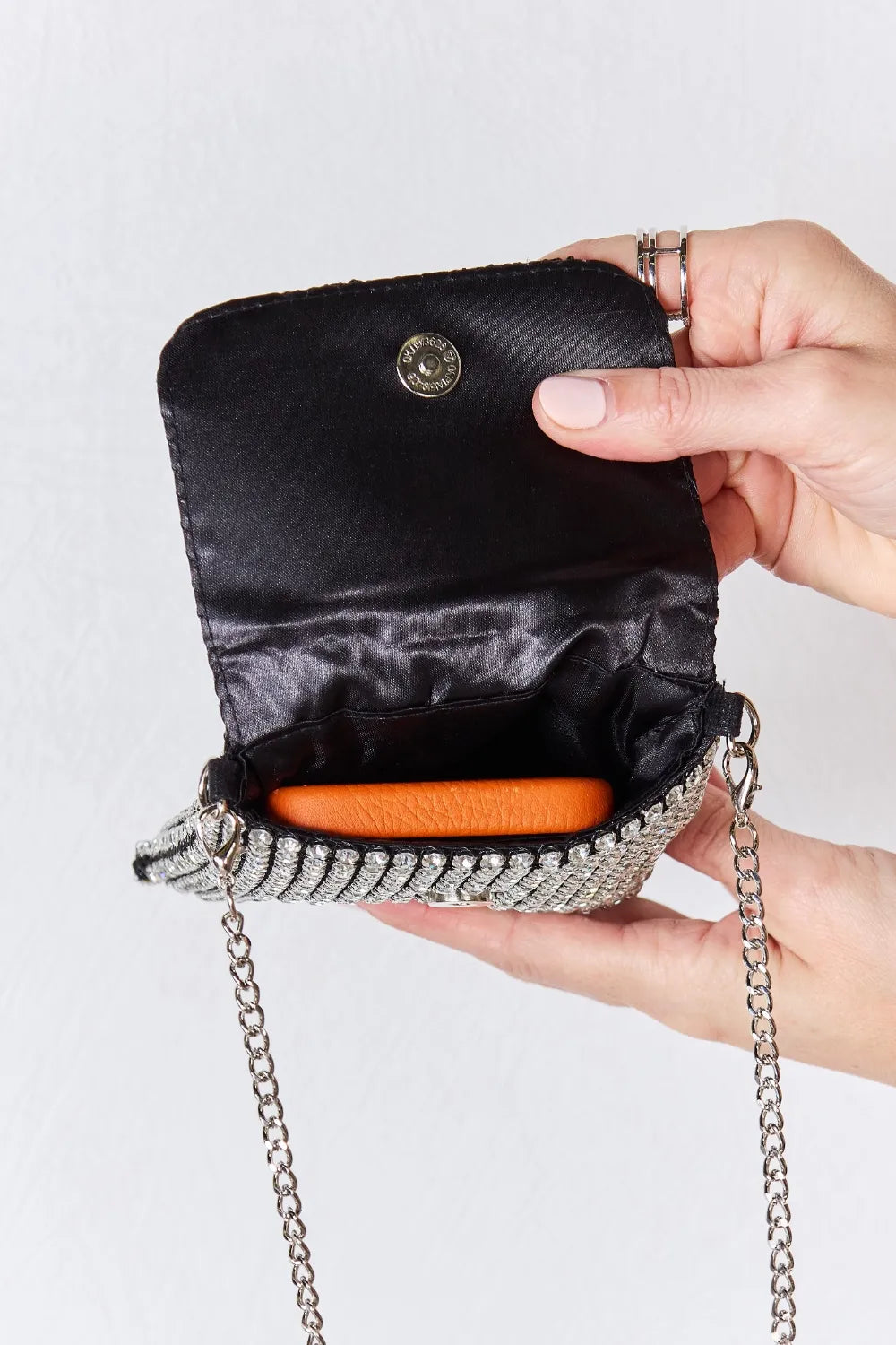 Rhinestone mini crossbody bag with black flap, silver chain strap, and orange interior