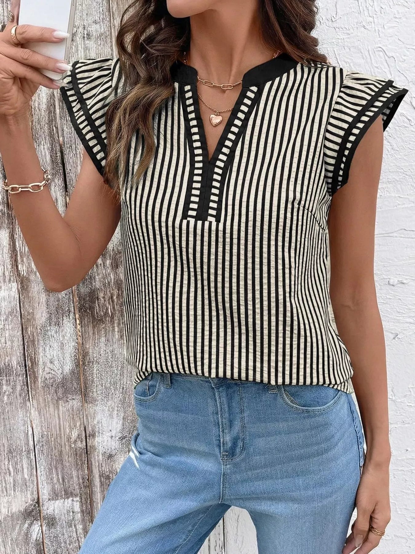 Striped ruffle-sleeve blouse in black and cream with black trim, paired with blue jeans.
