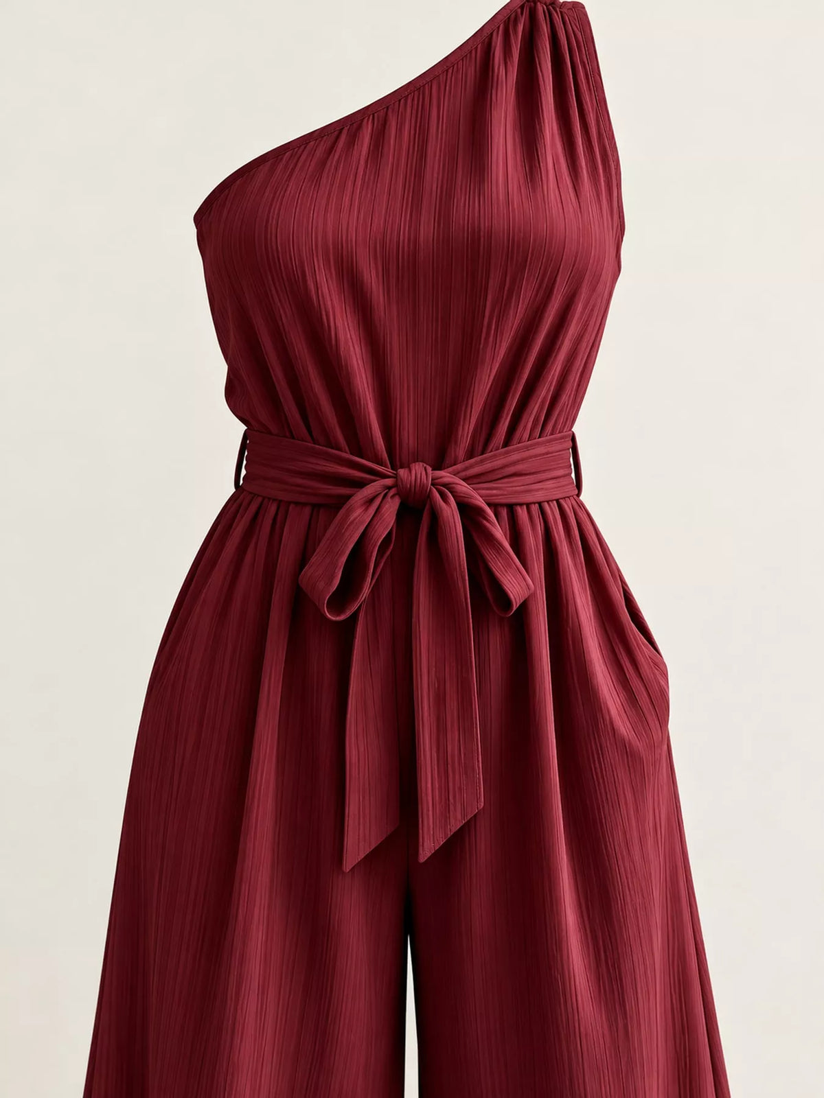 Burgundy one-shoulder jumpsuit with tie waist and textured pleated fabric