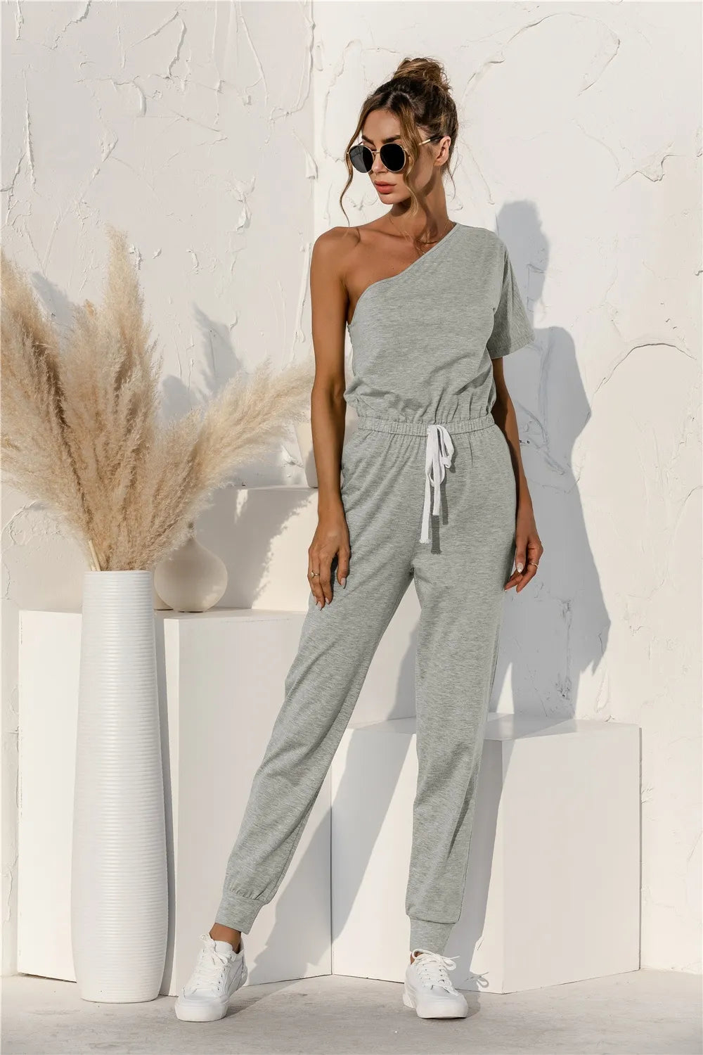 Gray single-shoulder short-sleeve jumpsuit with drawstring waist and relaxed tapered pants