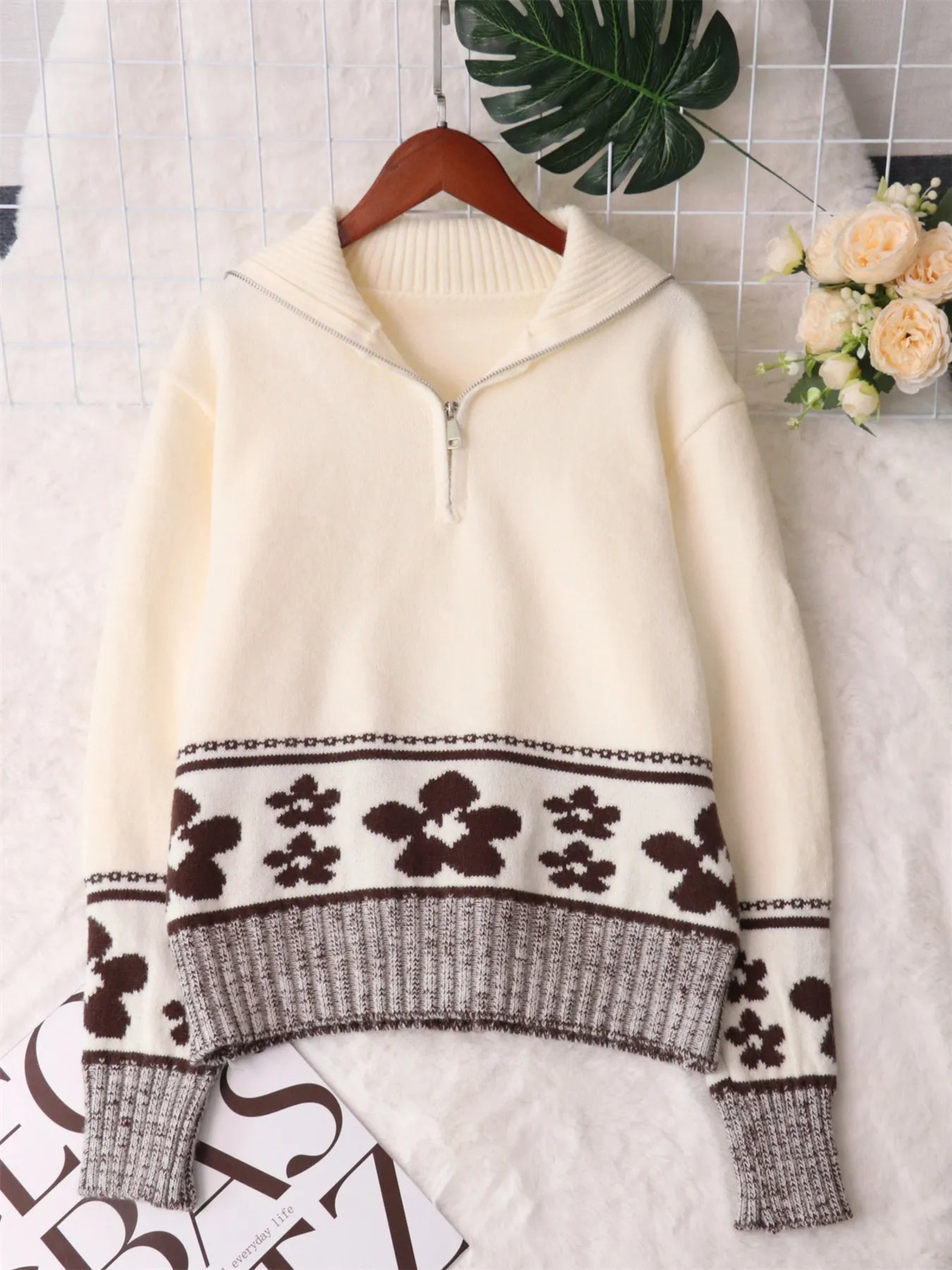 Cream sweater on hanger with high knit collar and black flower stripe at the midsection