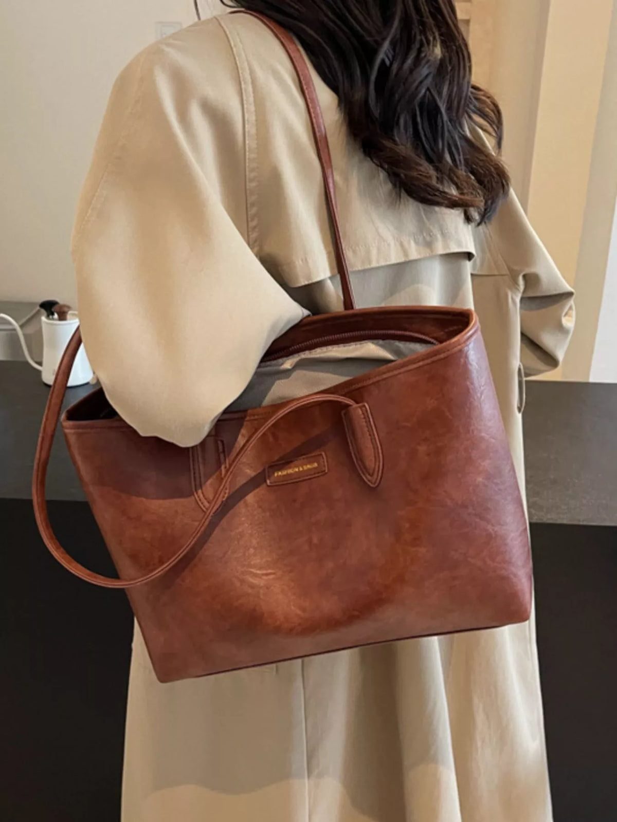 Brown vegan leather tote bag with front pocket, curved handles, and wide opening