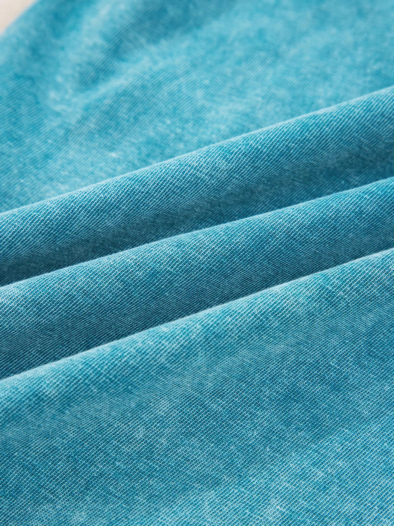 Teal fabric close-up showing mineral-wash texture on wide-leg pants