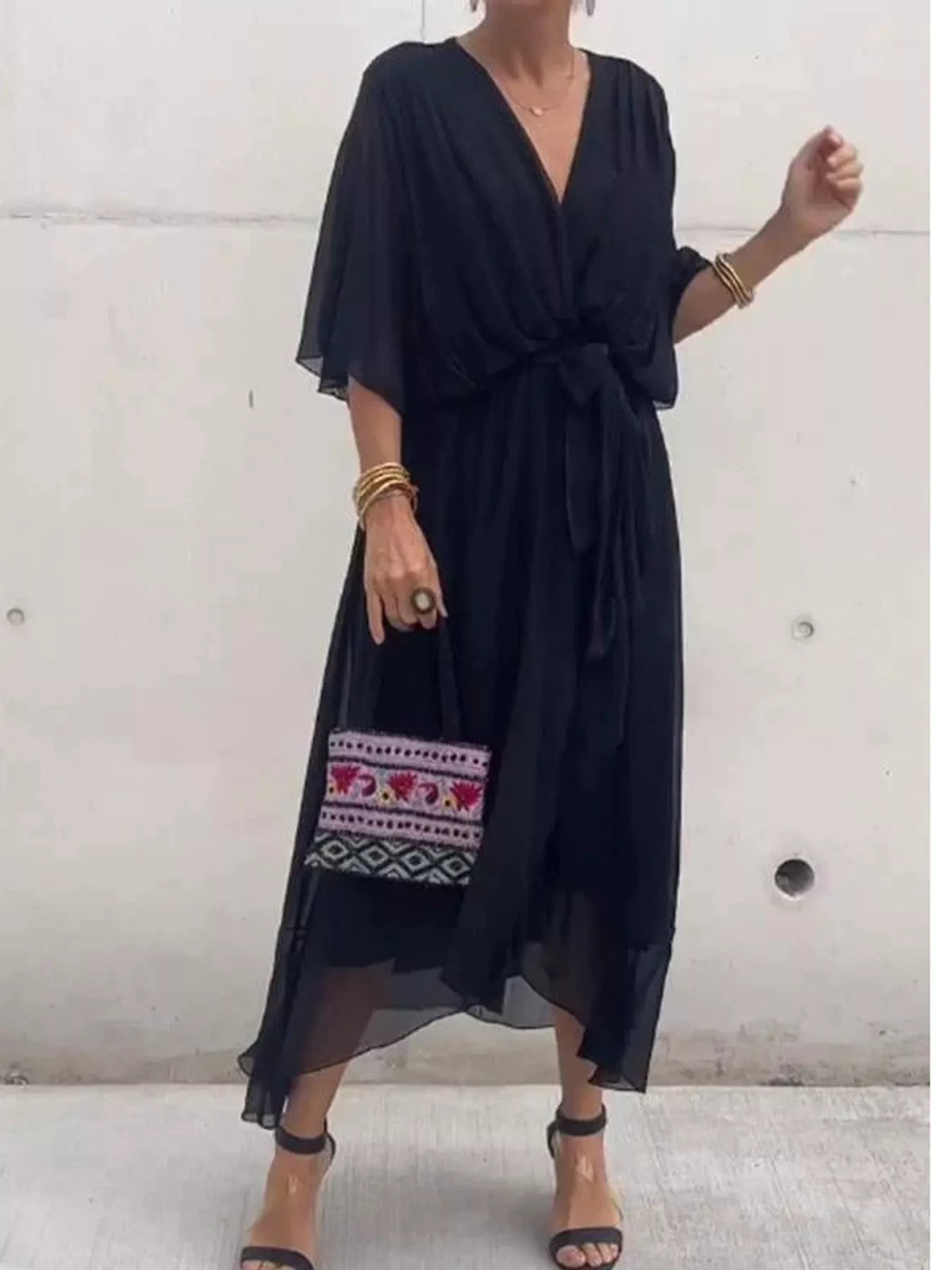Black wrap dress with ruched bodice, batwing sleeves, and waist tie; flowing midi length.