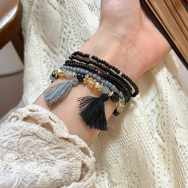 Beaded tassel rice bracelet with black, blue, and gold-tone charms, plus tassels
