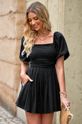 Black square-neck pleated romper with short puff sleeves and gathered skirt