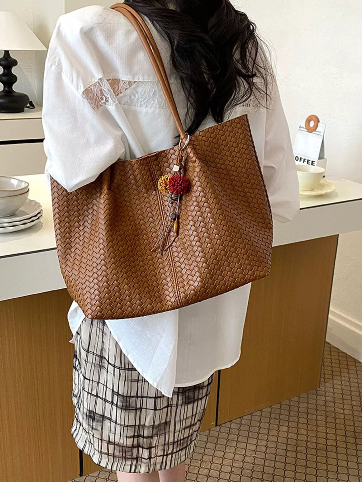 Brown woven vegan leather tote bag with long handles and dangling floral tassel charm