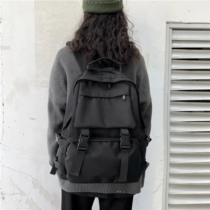 Black backpack worn by person, front flap pocket and adjustable shoulder straps