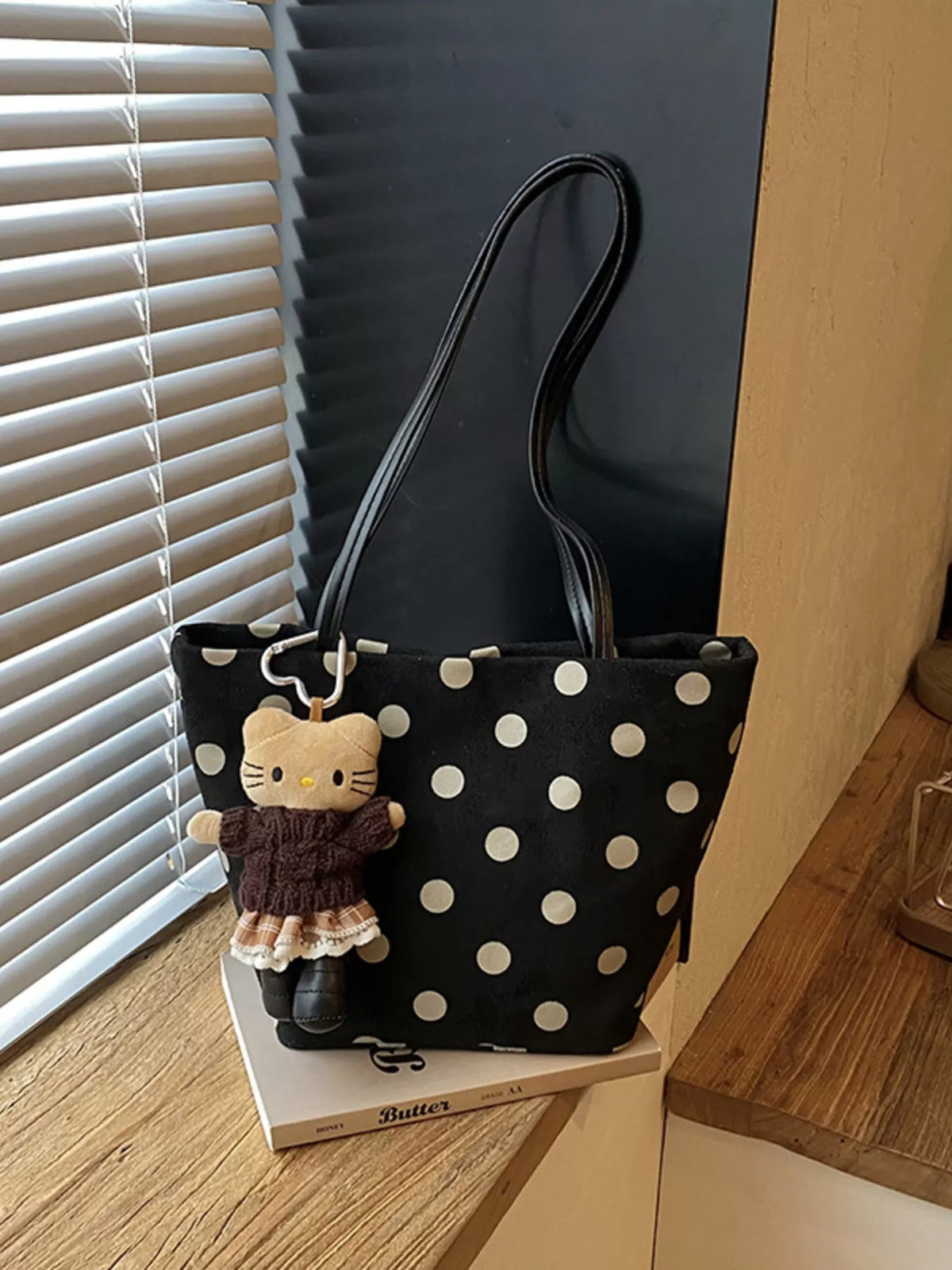 Black polka dot suede shoulder handbag with rounded top and cute cat charm