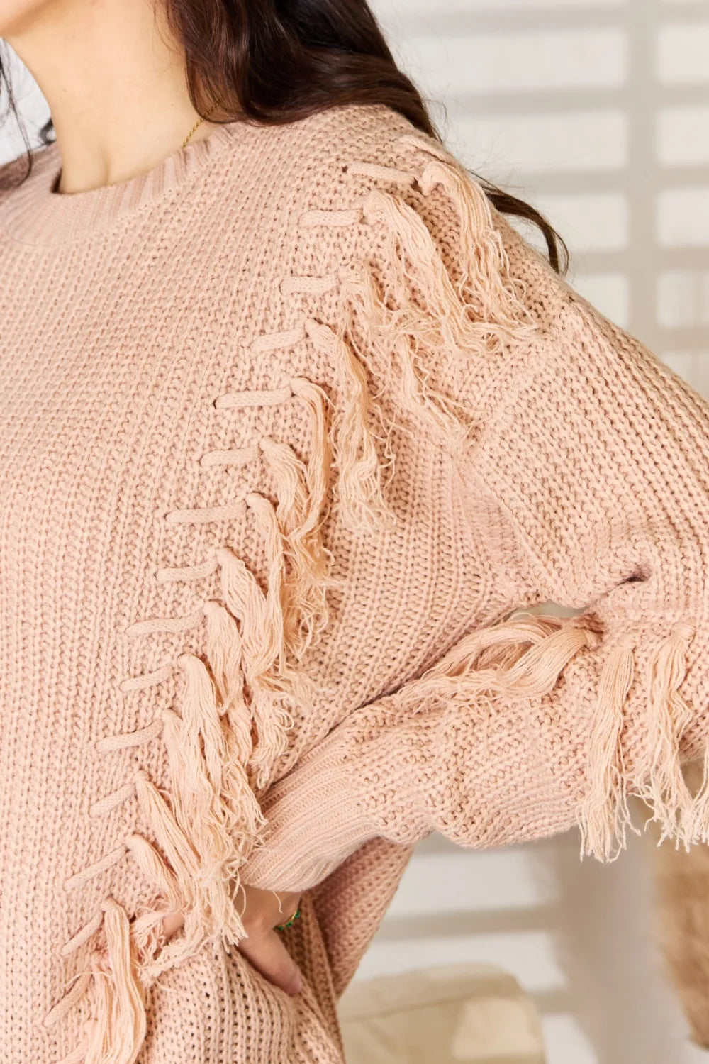 Dusty pink knit sweater close-up with fringe tassel trim along shoulder seam