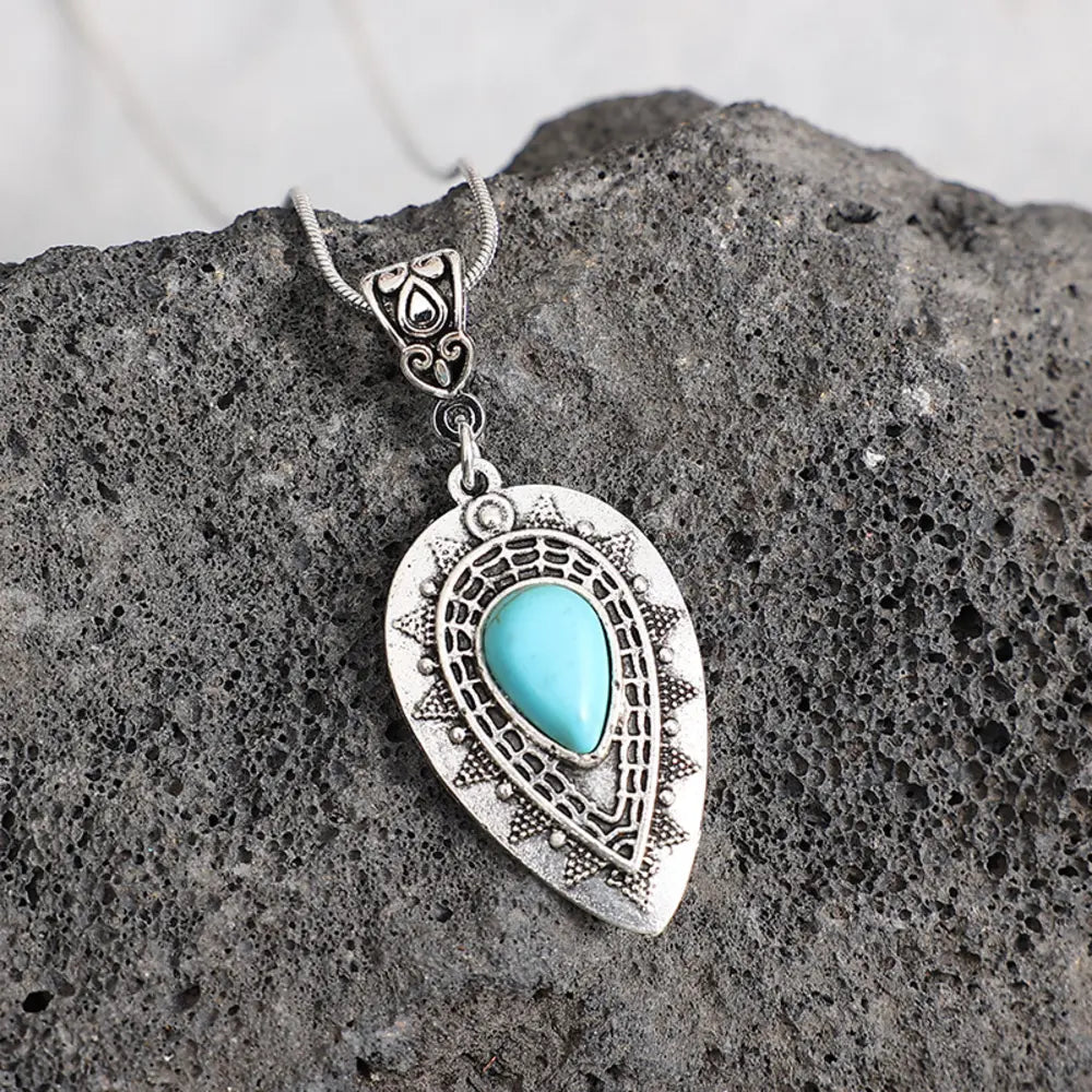 Silver pendant necklace featuring ornate teardrop charm with turquoise blue stone