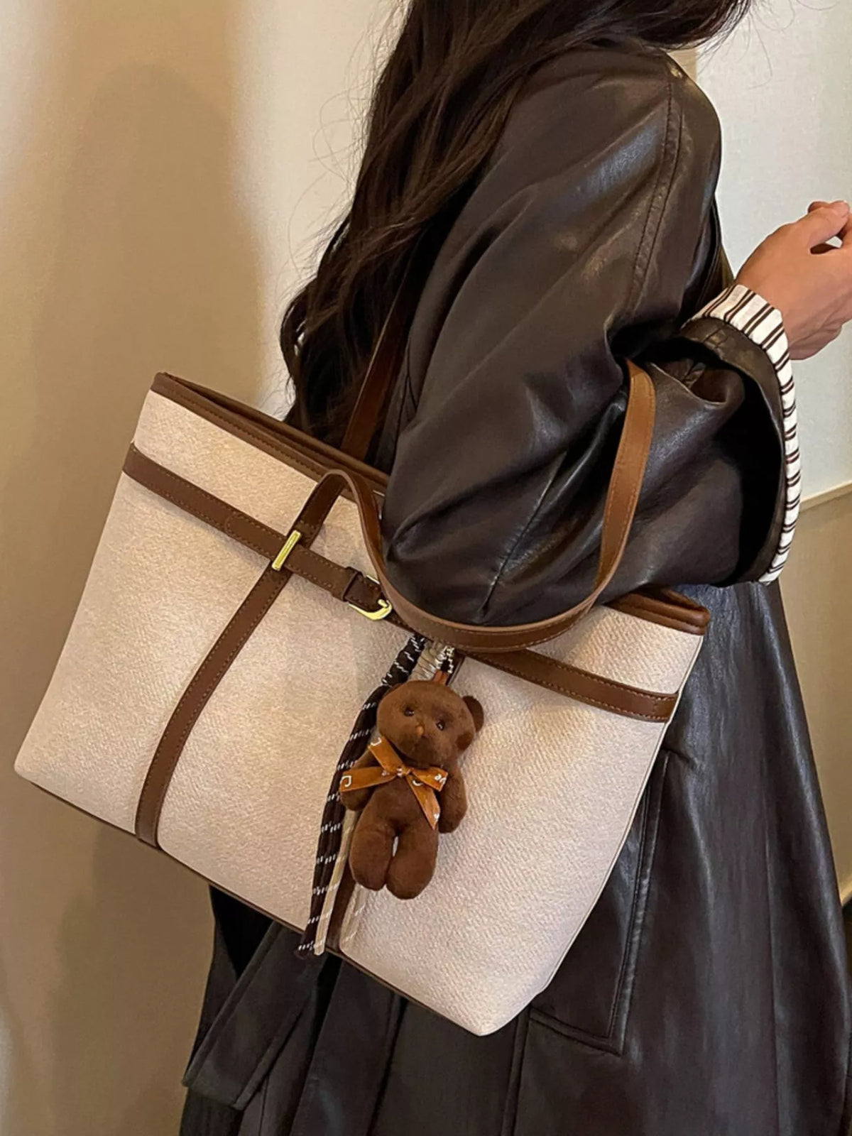 Off-white tote bag with brown trim, teddy keychain charm, and striped hanging tassel