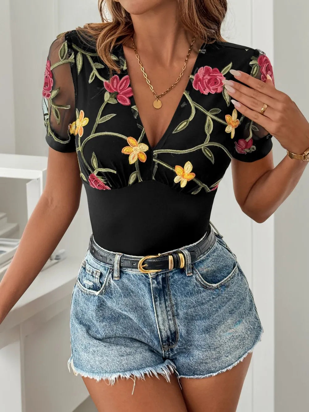 Black floral embroidered V-neck bodysuit with sheer sleeves and fitted high-cut leg