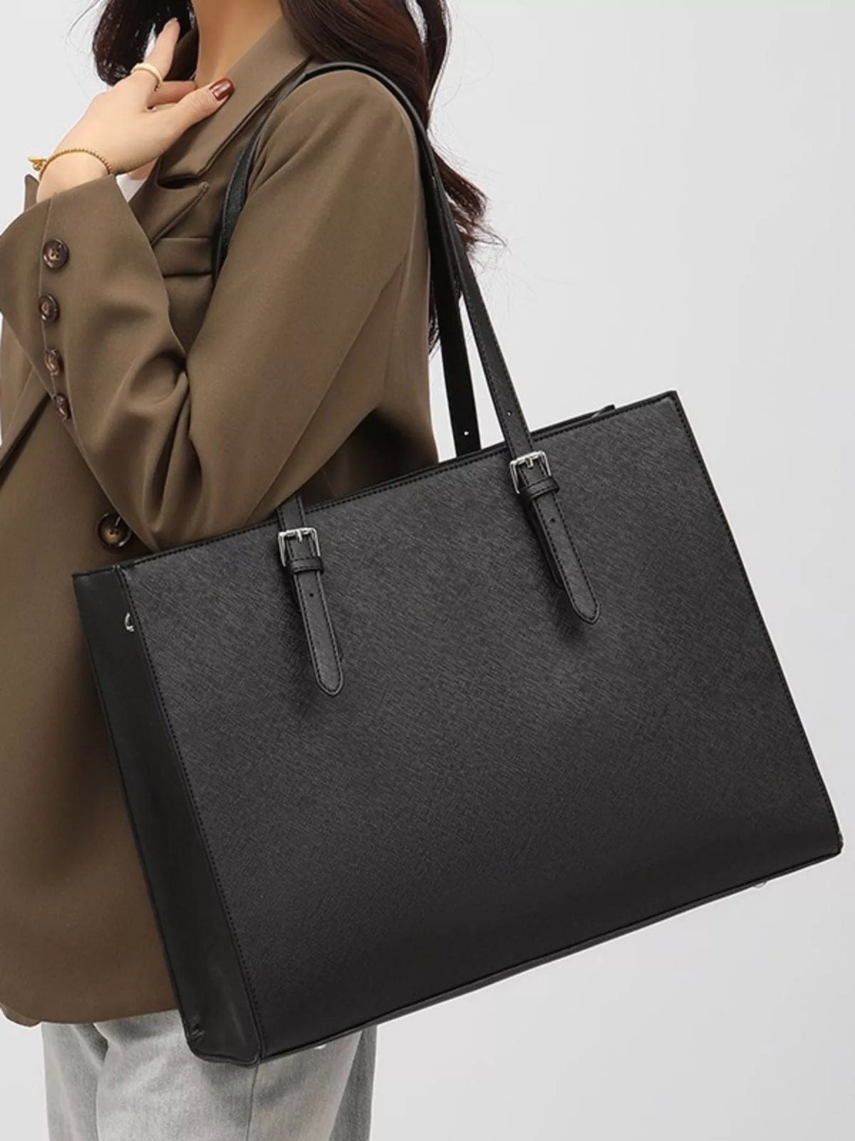 Black large tote bag with two top handles, front strap details, and adjustable shoulder strap.