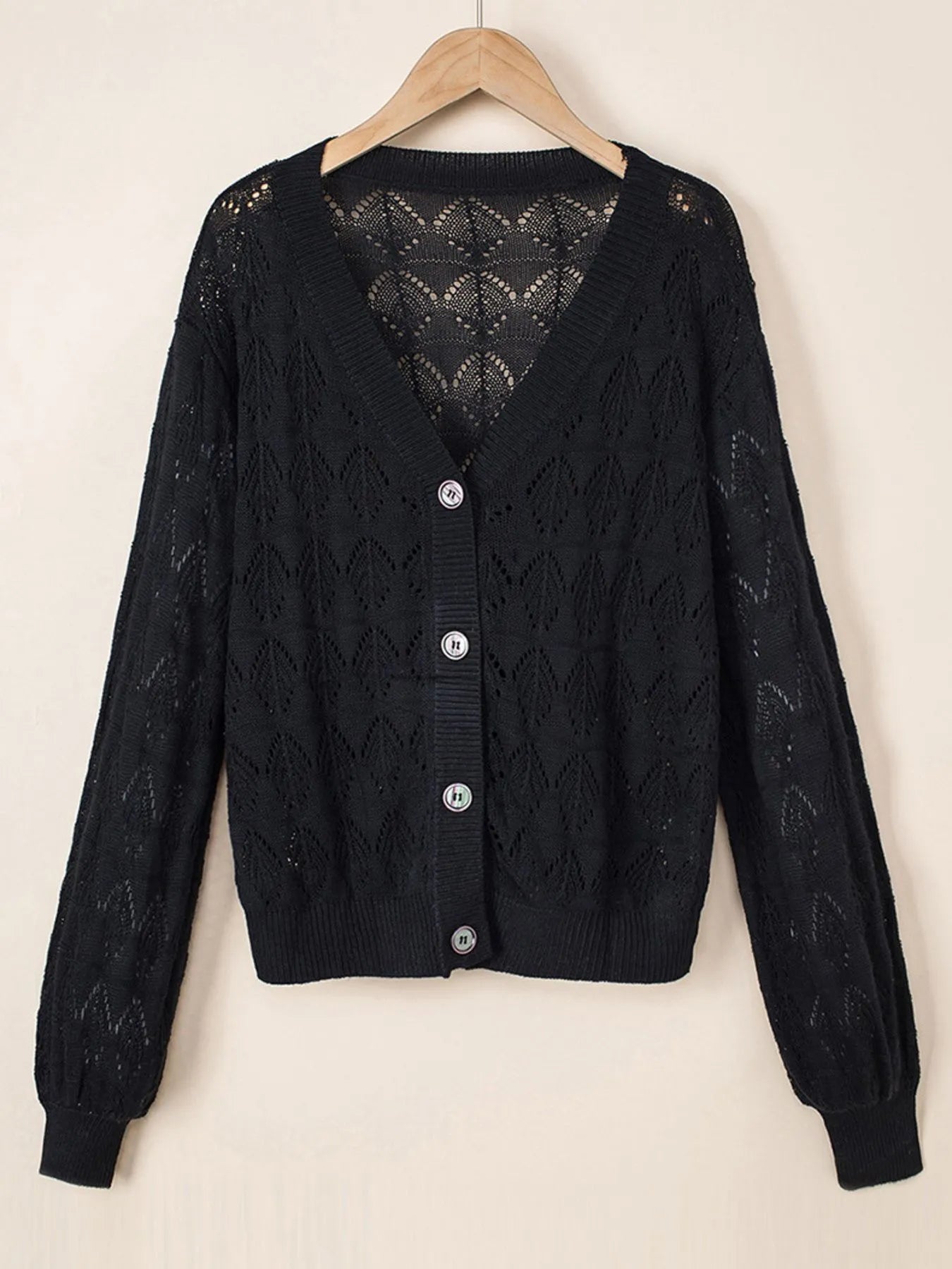 Black openwork button-up cardigan with V-neck and long sleeves, hanging on hanger