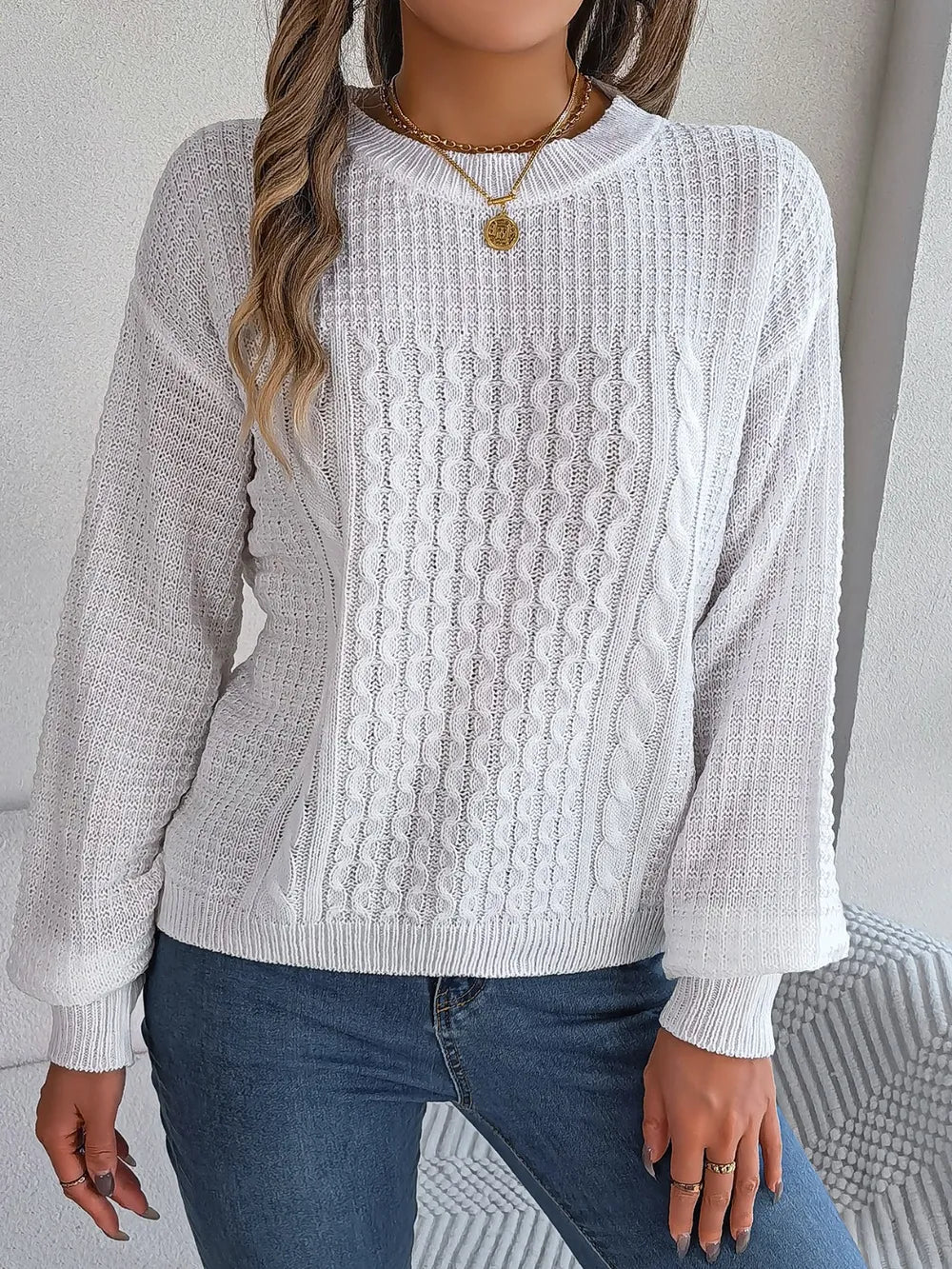 White cable-knit sweater with round neck, long sleeves, and raised cable texture.