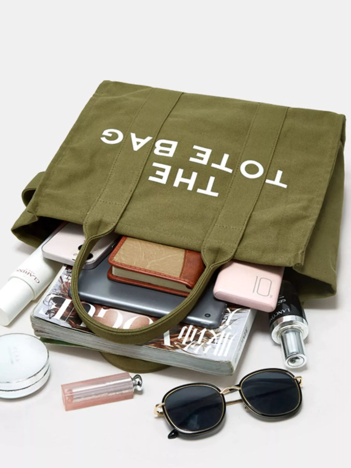 Army green canvas tote bag with “THE TOTE BAG” print, folded top with items