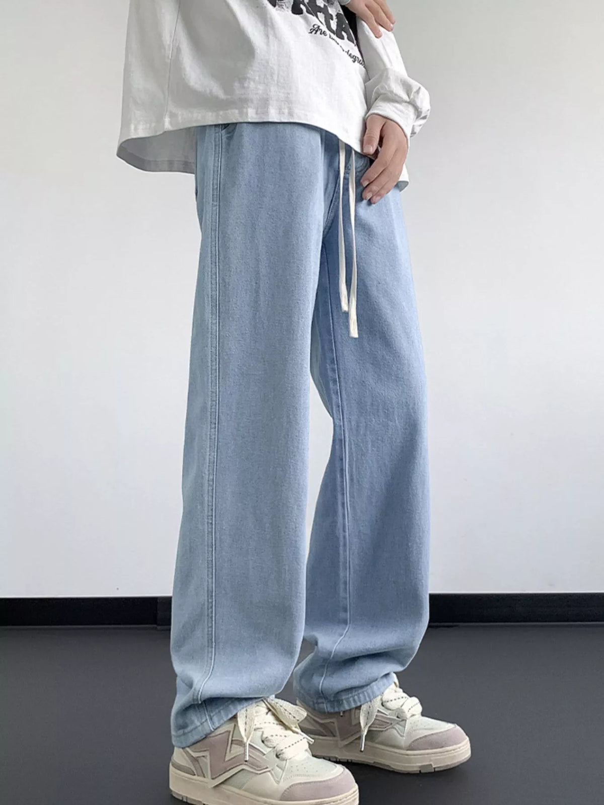 Light blue washed denim jeans with relaxed fit, wide legs, and hanging drawstring ties