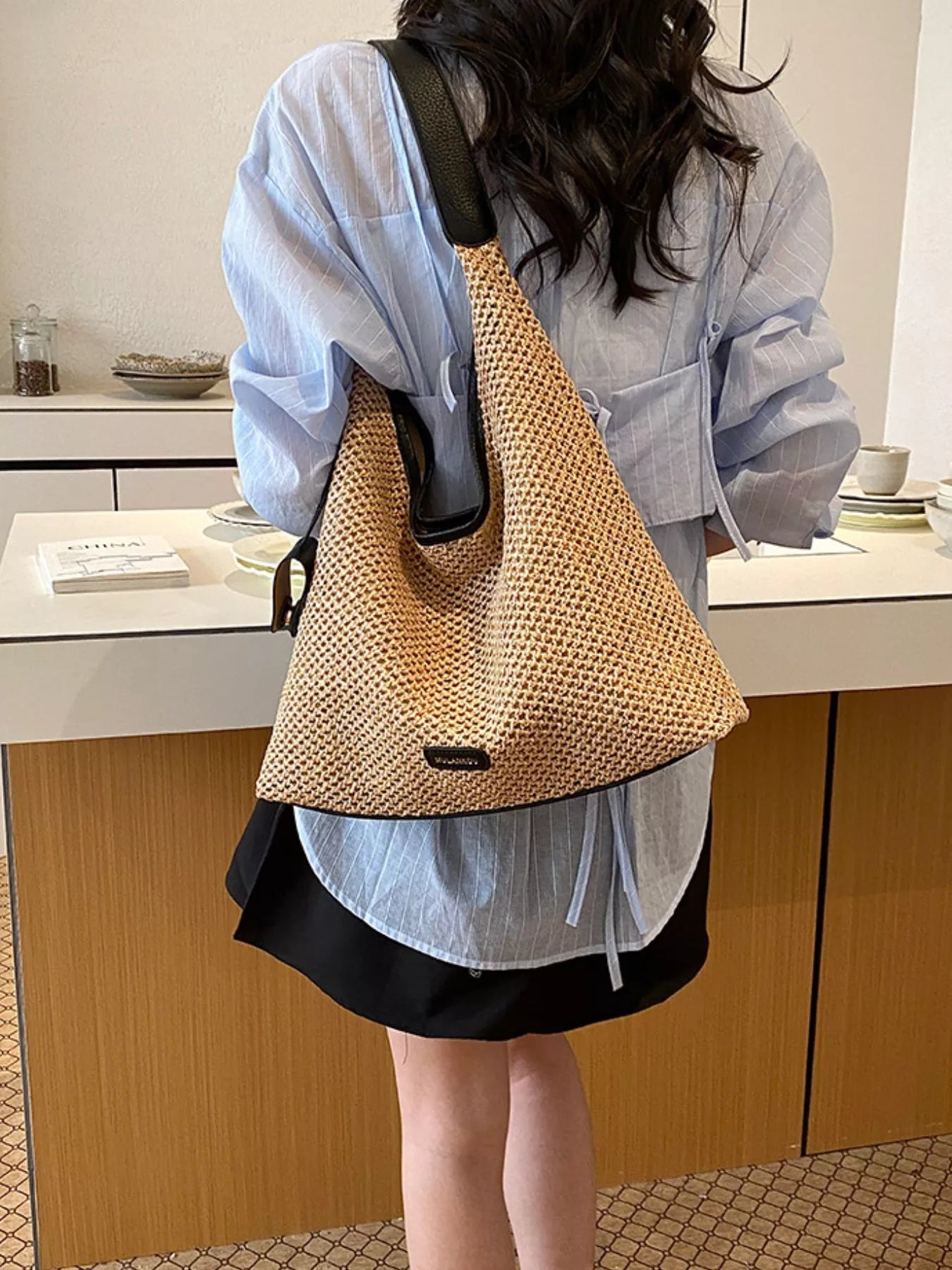 Camel woven straw shoulder bag with black handle and small rectangular logo plate