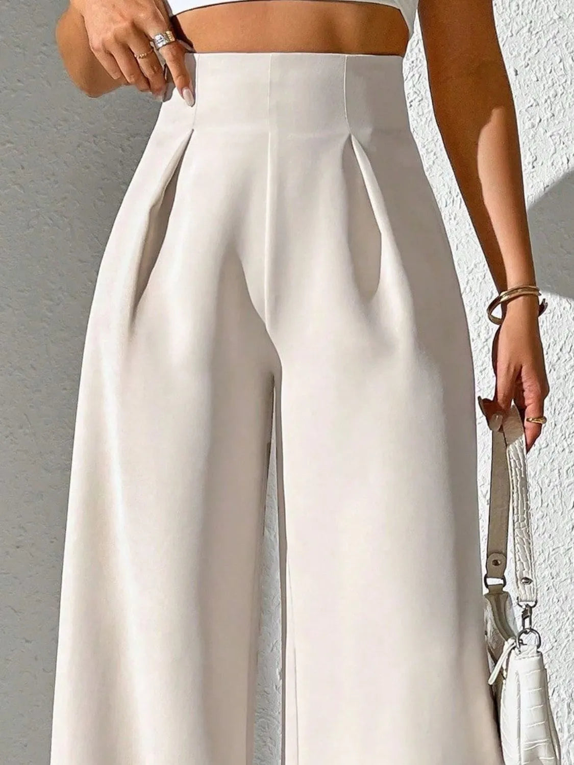 Beige high-waist wide-leg pants with prominent pleats at the waistband