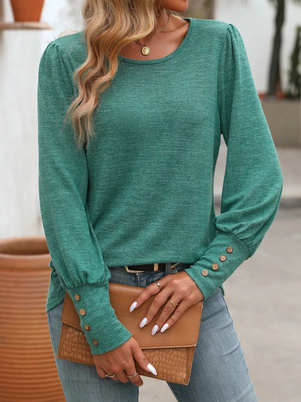 Deep teal round-neck long-sleeve t-shirt with decorative button cuffs.