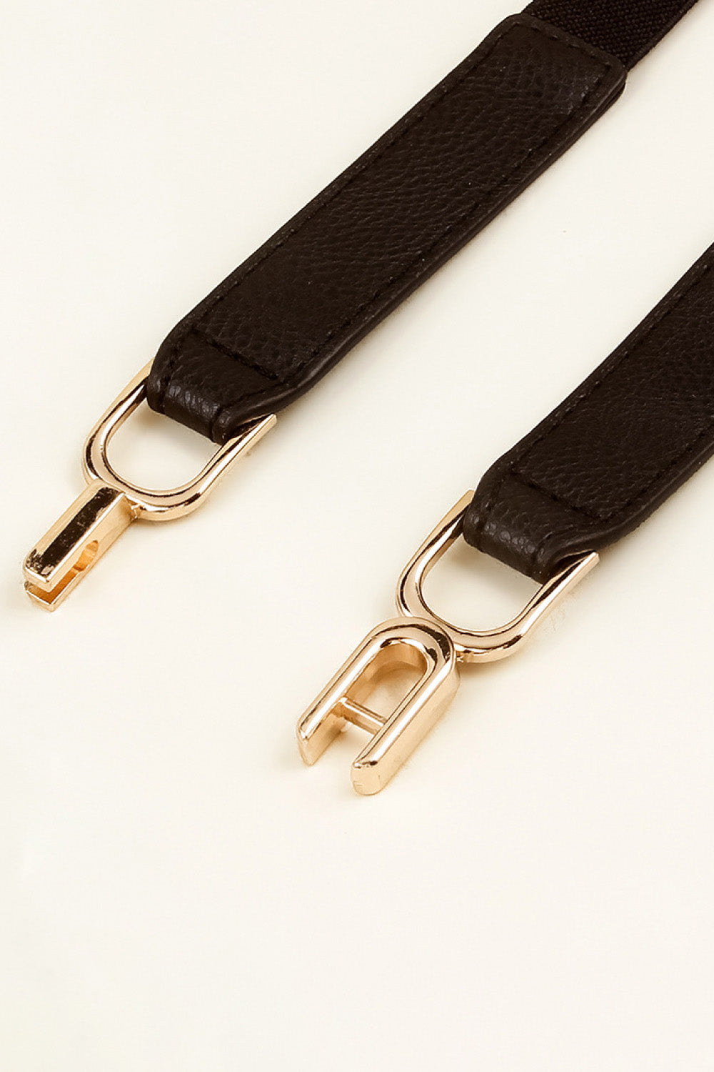 Black elastic belt with gold-tone buckle hooks and stitched leather strap ends