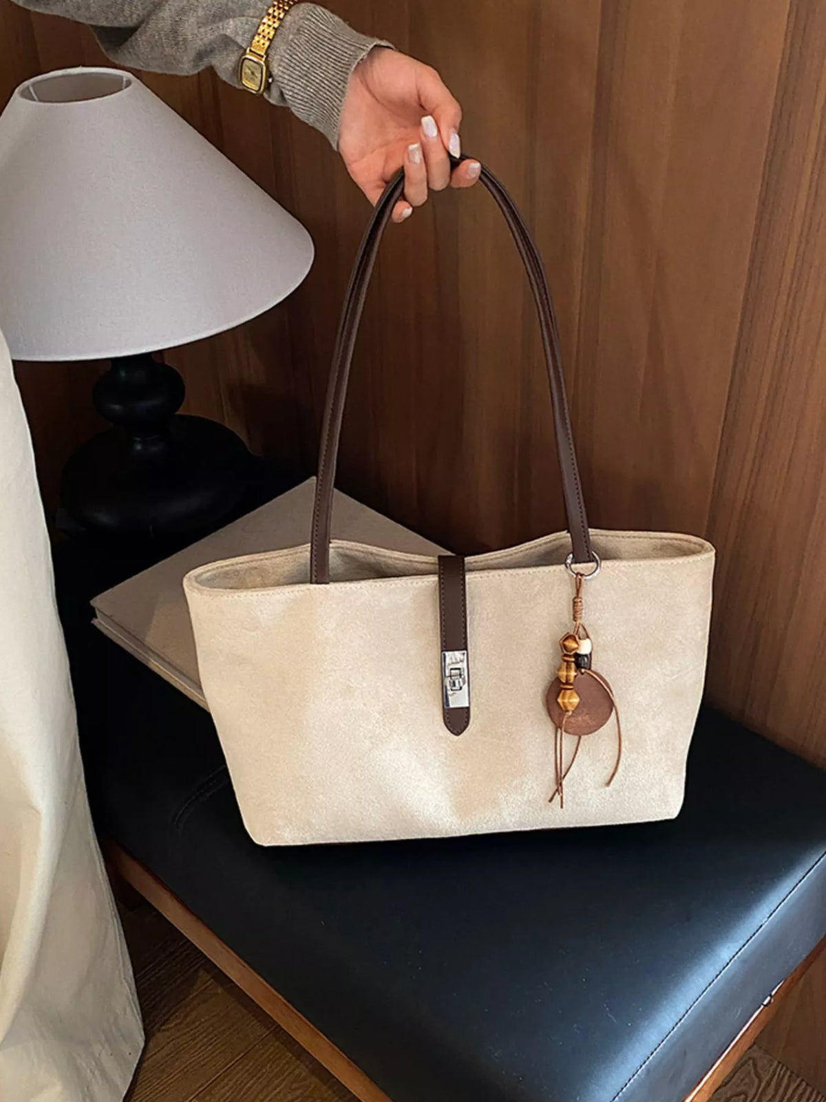Beige suede medium tote bag on a seat, featuring top handles and buckle detail