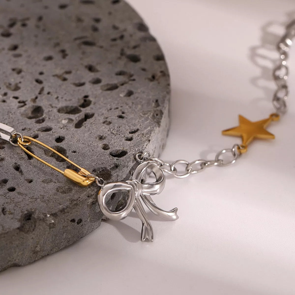 Two-tone star bow necklace close-up: silver chain with gold bar link and ribbon bow charm
