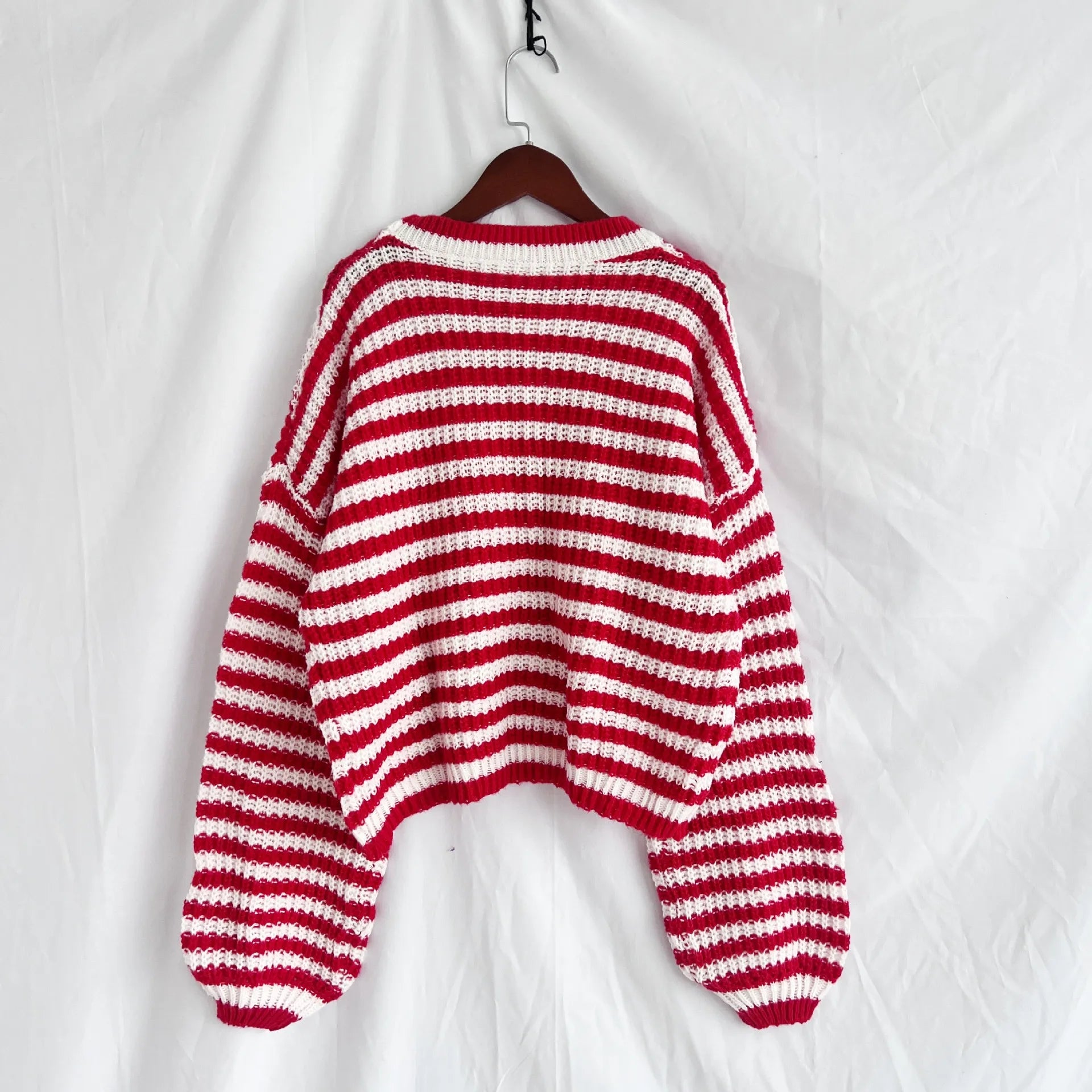 Red and white striped oversized knit sweater, back view, hanging on a wooden hanger