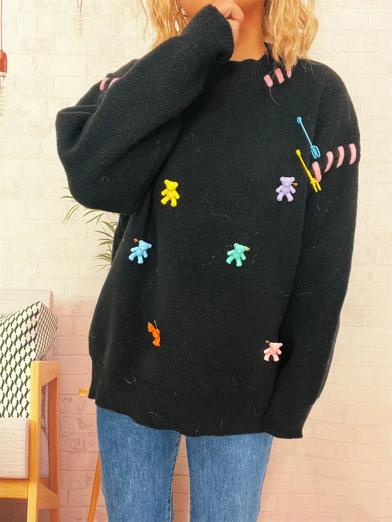 Black round-neck knit sweater with colorful animal appliques, hand near neck