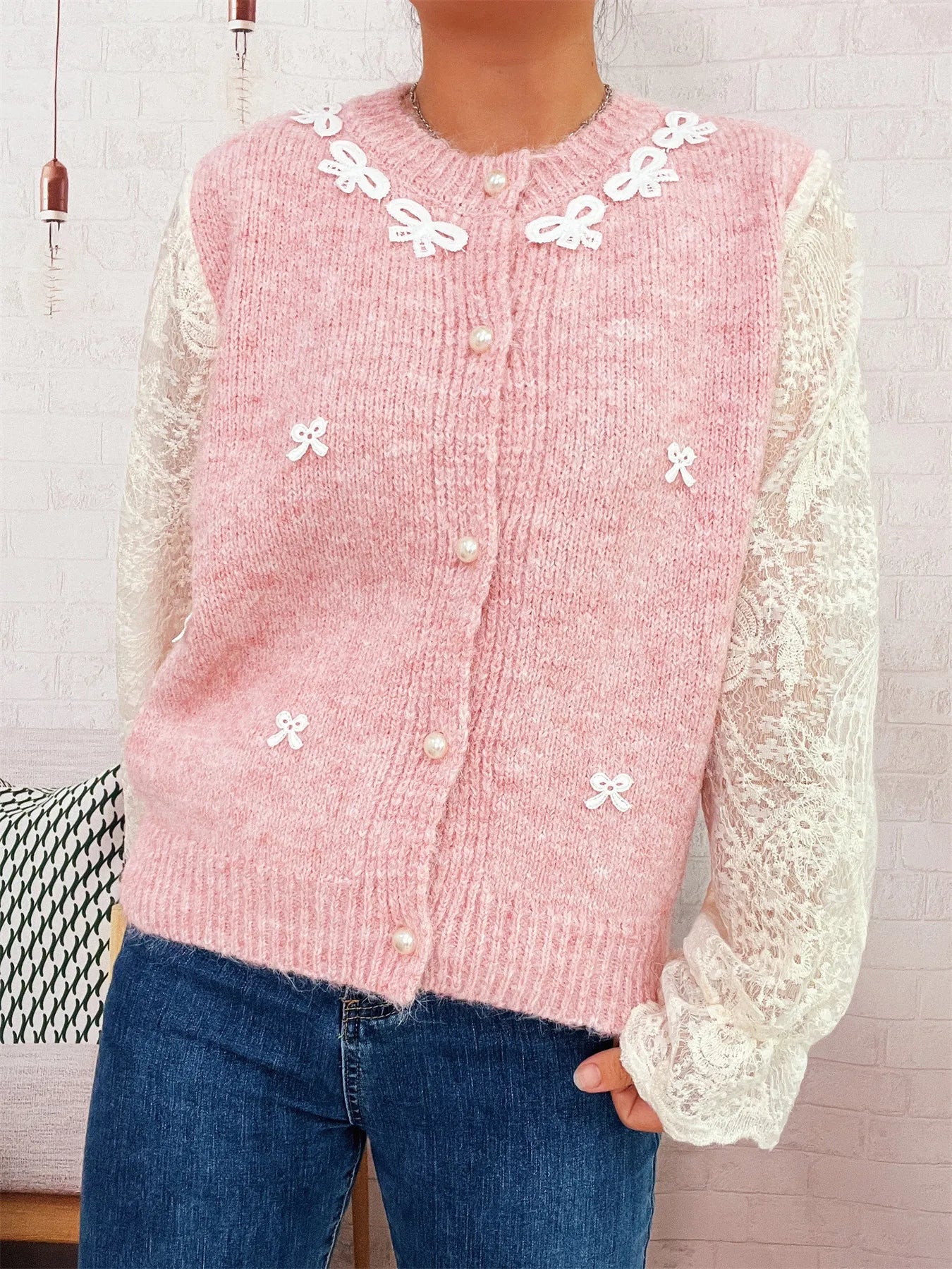 Pink knit button-up cardigan with lace sleeves and white bow appliques at neckline