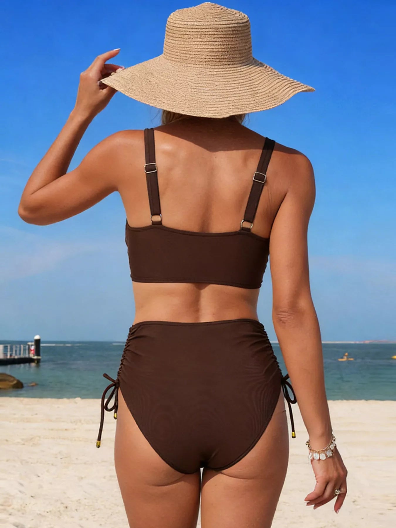 Crisscross High-Waisted Swim Set in brown with adjustable shoulder straps on model at the beach