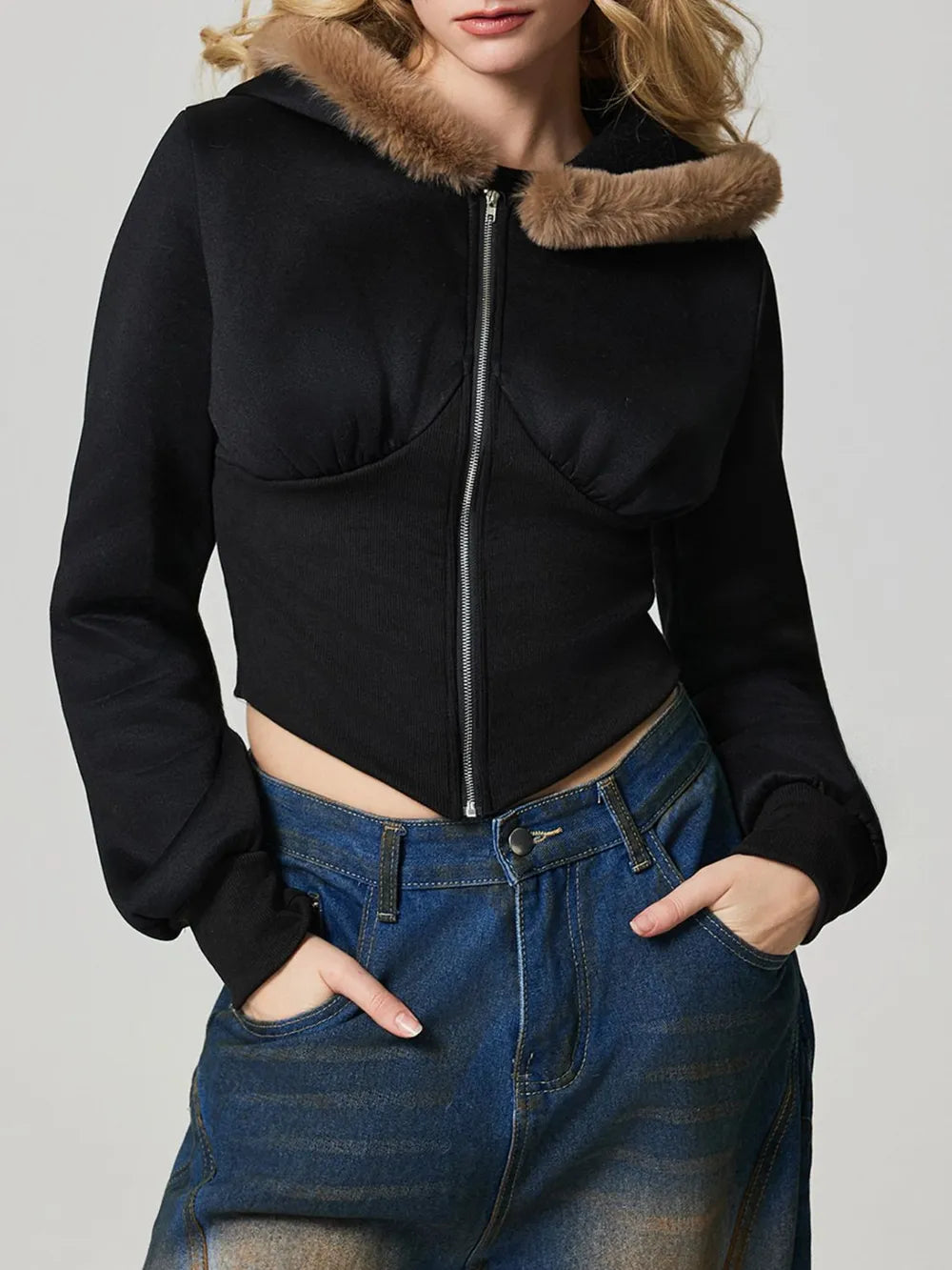 Black cropped zip-up jacket with fuzzy hood trim, front zipper, and long sleeves over denim.