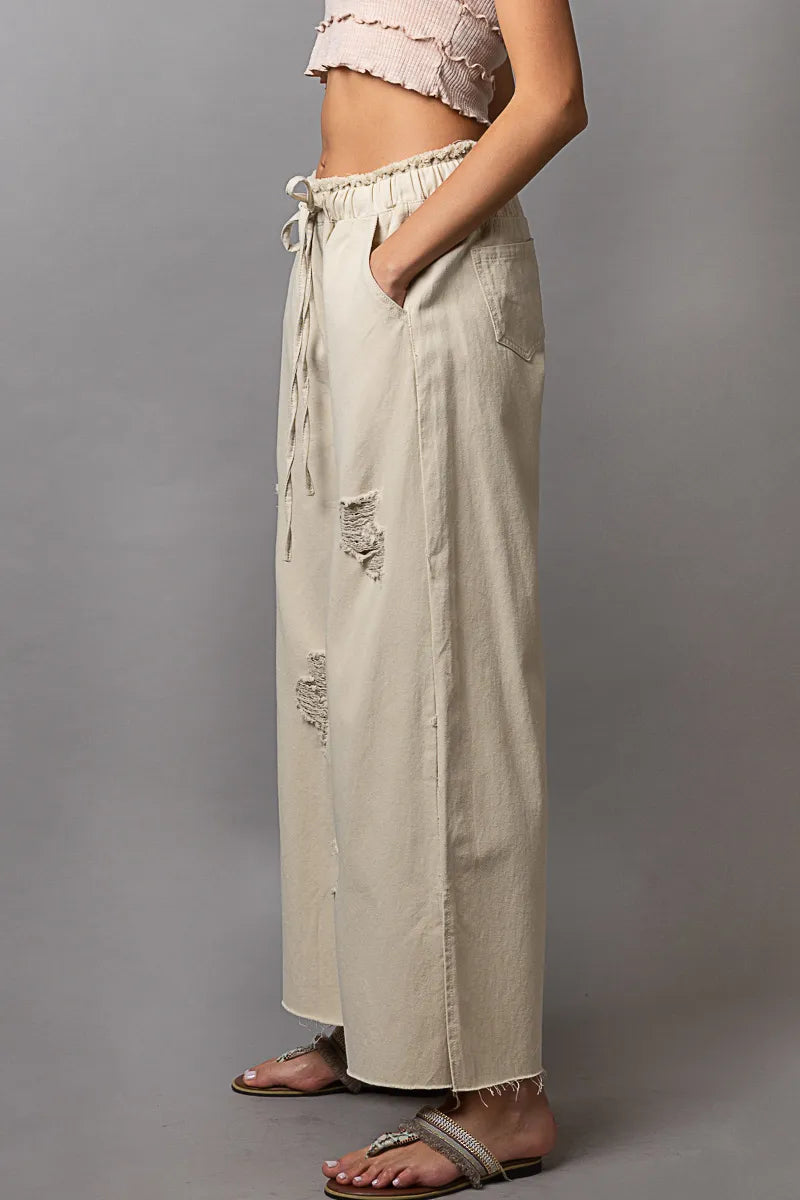 Cream wide-leg drawstring pants with distressed patches and frayed cuffs