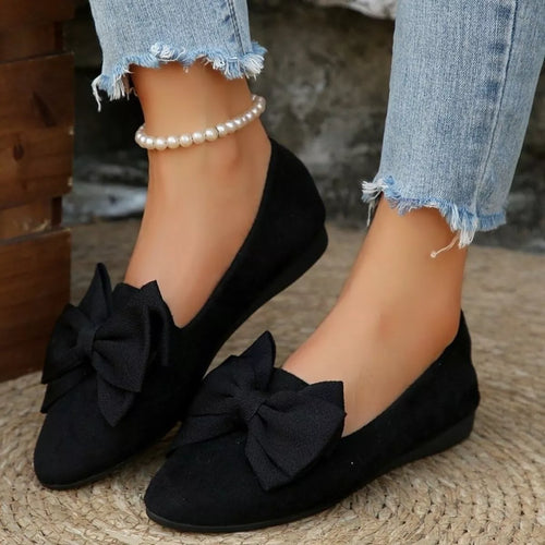 Black bow point-toe slip-on shoes on feet with oversized front bow