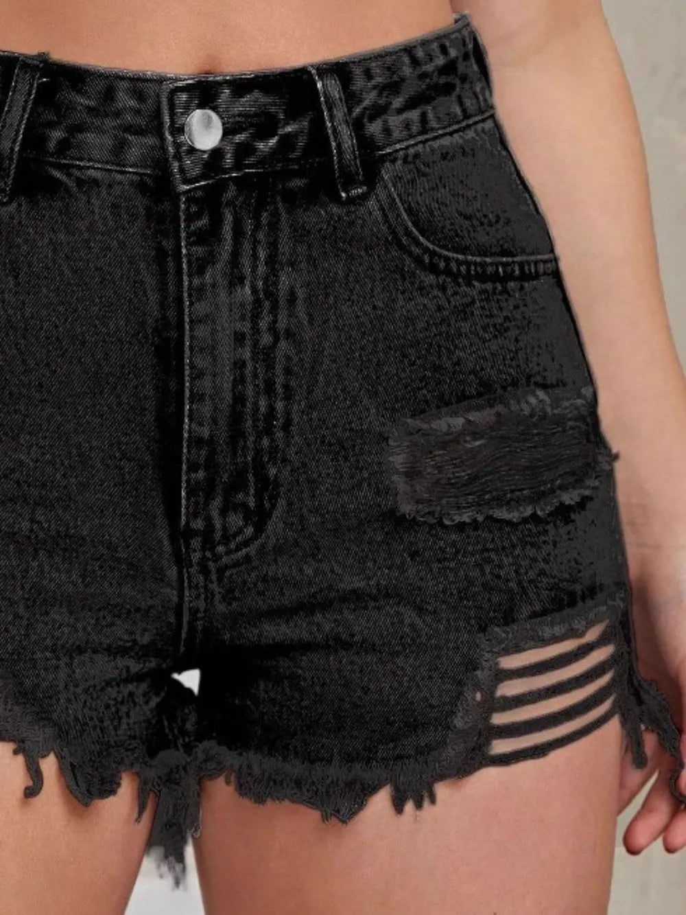 Black high-waist denim shorts close-up with distressed patches and frayed raw hem