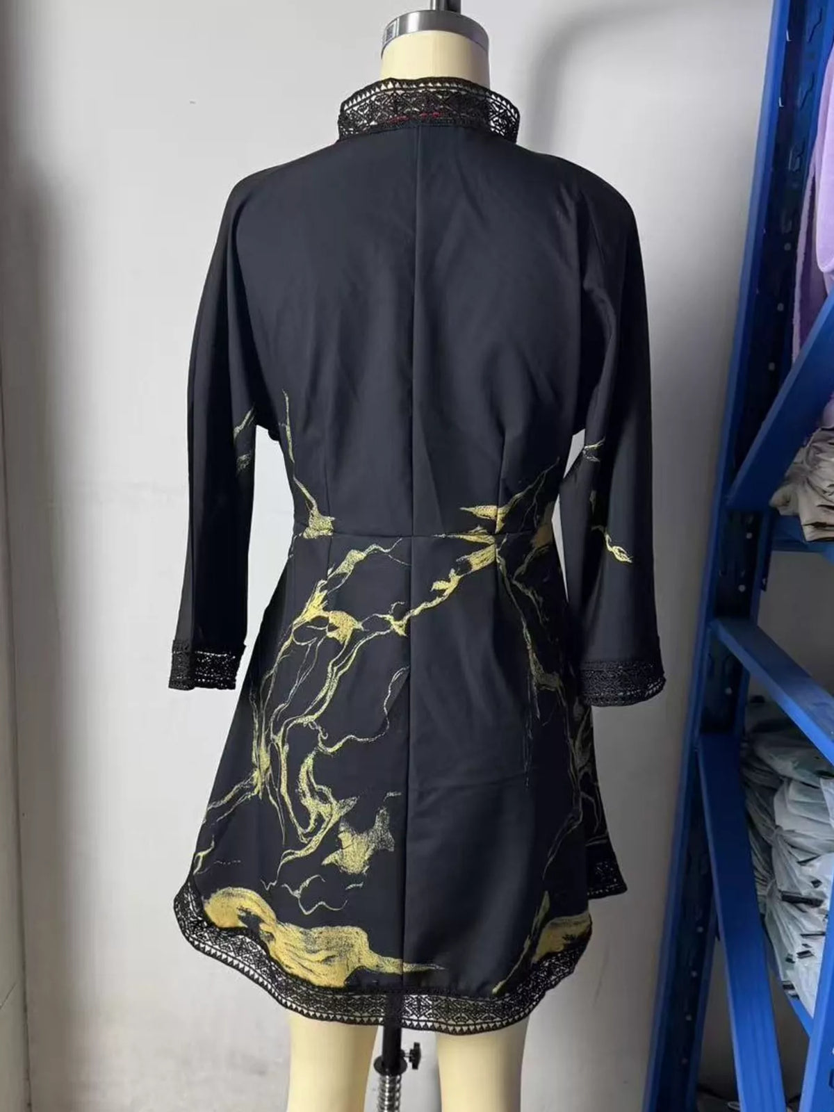 Black mini dress on mannequin, back view with gold abstract print and lace-trim border