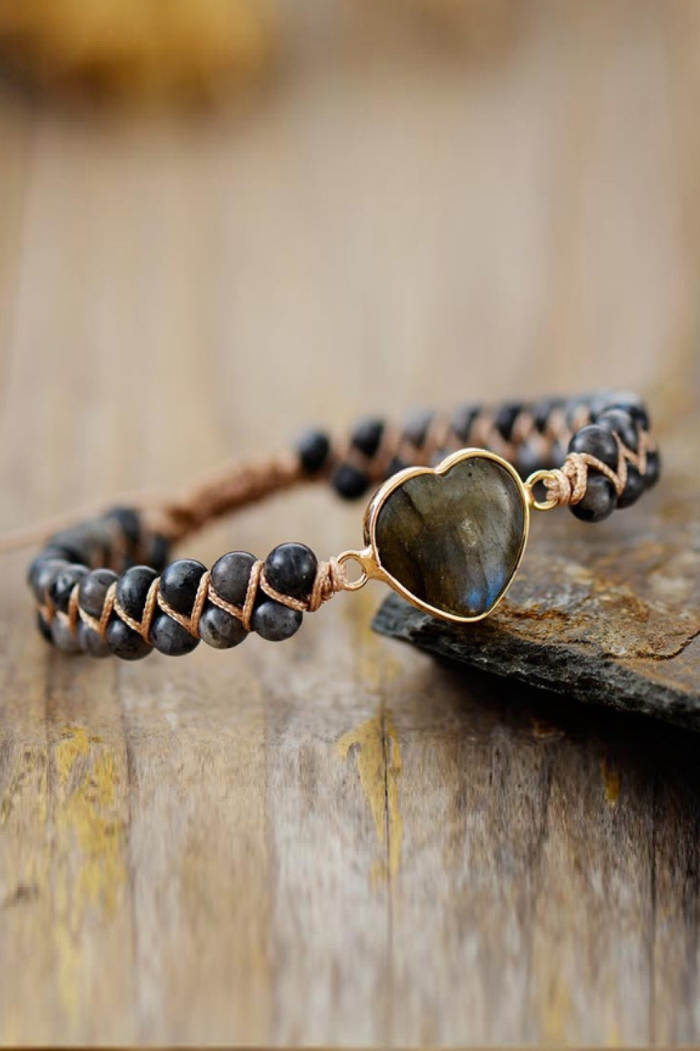 Dark braided bracelet with gold-tone clasp and heart-shaped gray stone pendant