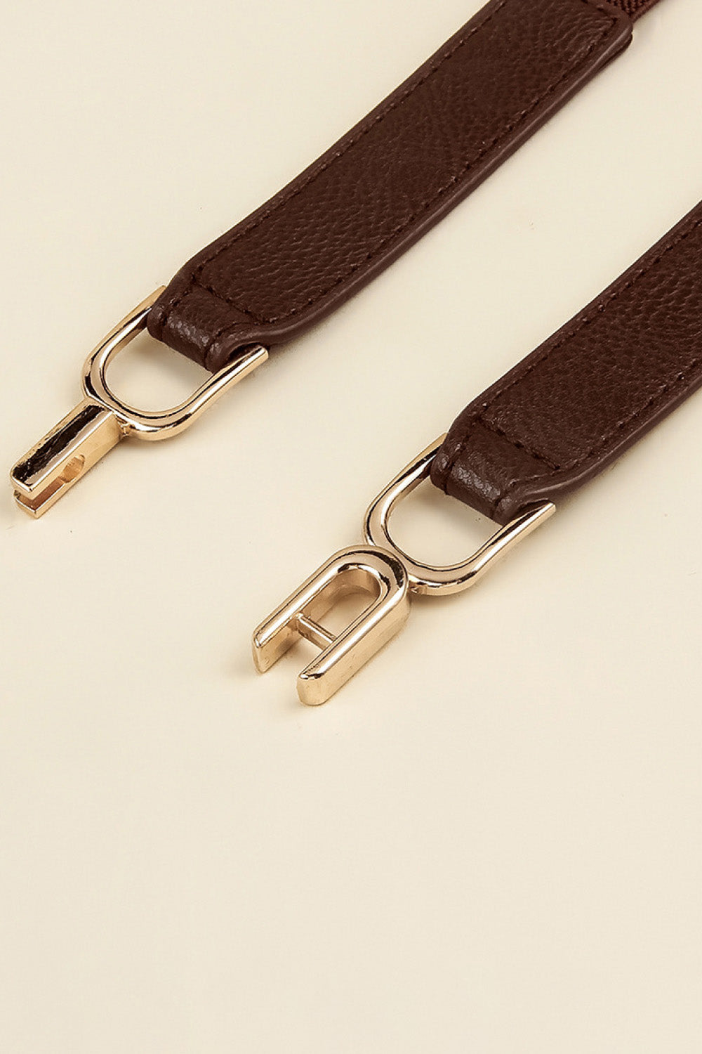 Close-up of dark brown elastic belt strap with gold-tone buckle and loop