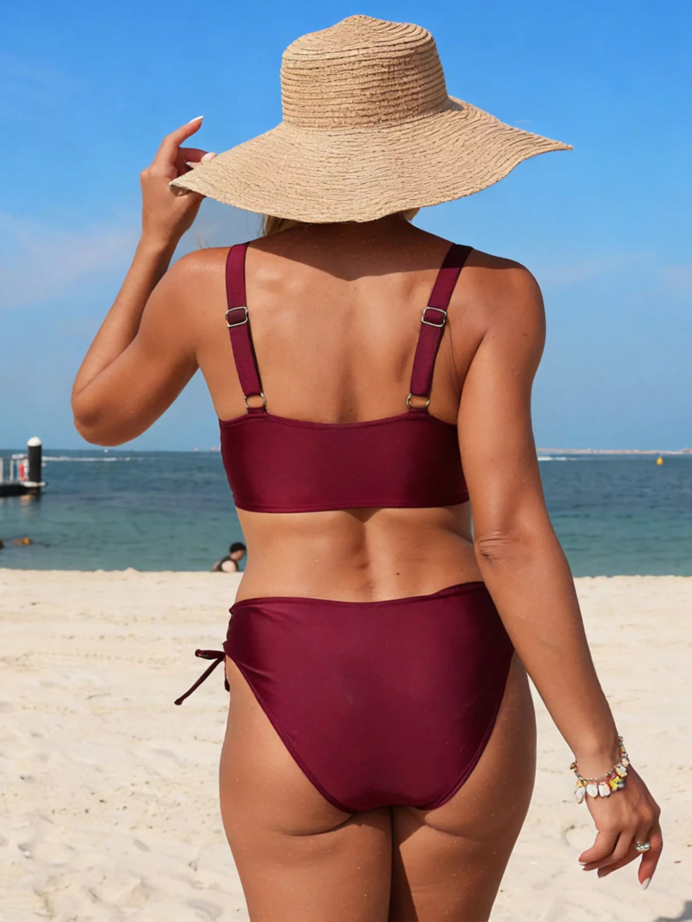 Palm Tree Cutout Lace-Up Swim Set two-piece burgundy bikini on beach model with straw hat (back view)