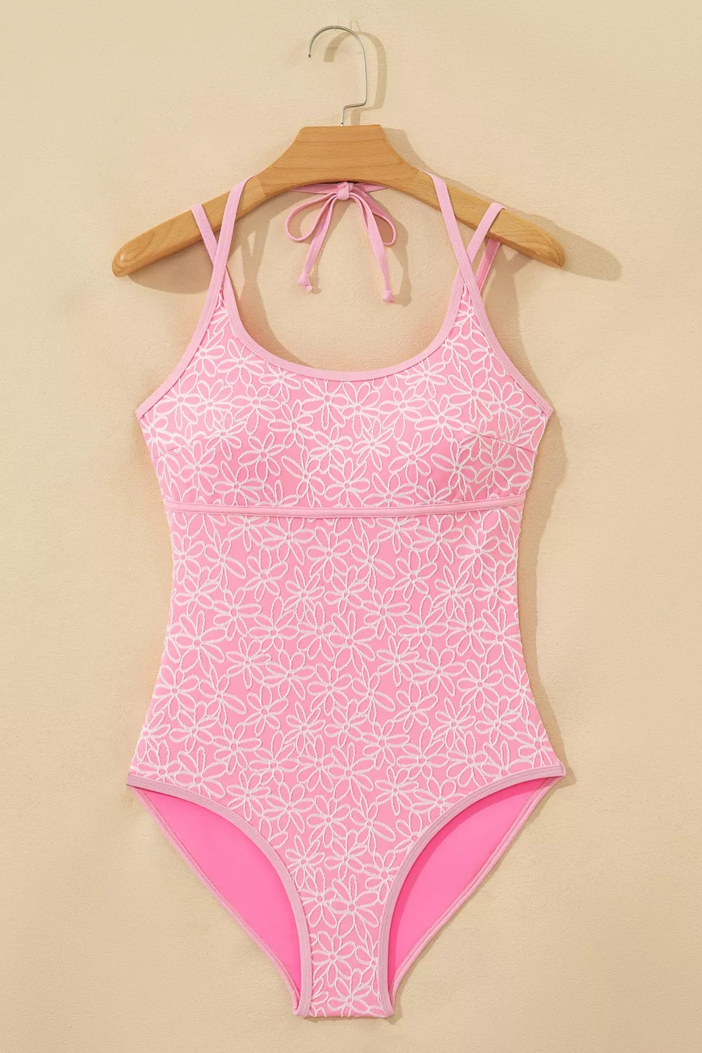 Blush pink floral halter one-piece swimsuit on wooden hanger, adjustable tie straps