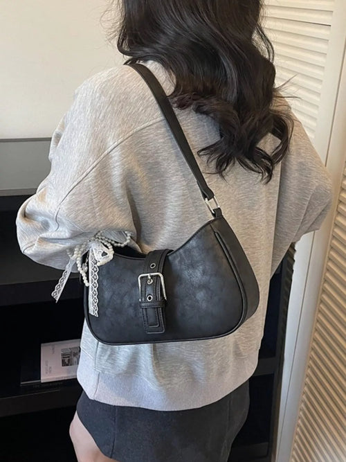 Black shoulder bag with adjustable strap and front buckle detail, worn over jacket