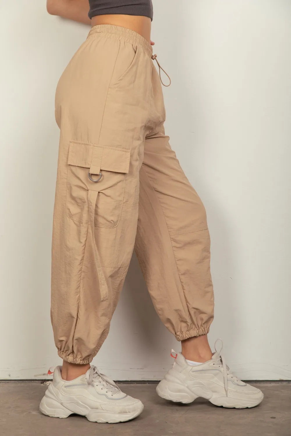 Taupe cargo pants with large flap pocket, elastic waist, and drawstring ankle cuffs