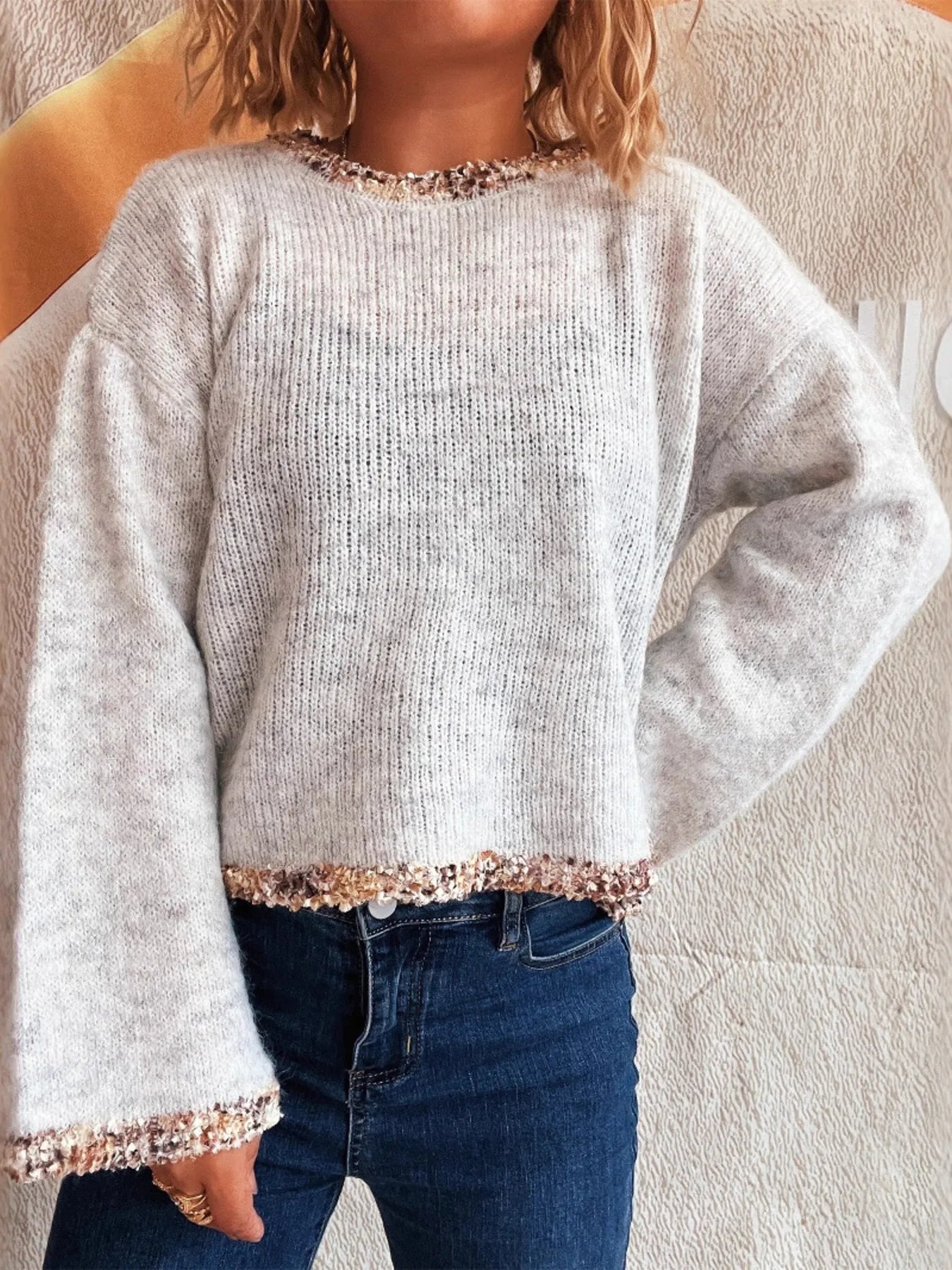 Light gray cropped sweater with round neck and sparkly trim on cuffs and hem, side view