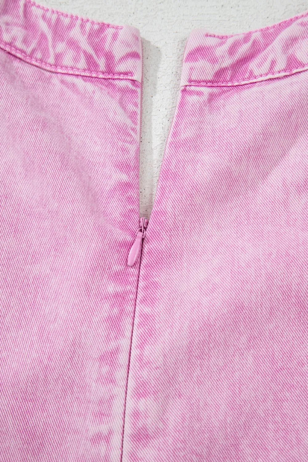 Pink mineral-wash denim romper back close-up with bow tie at center