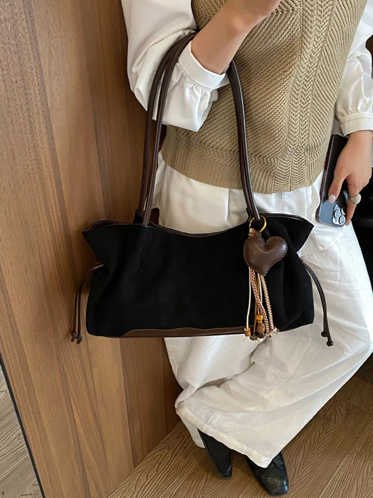 Black suede drawstring shoulder bag worn crossbody, with heart charm and tassel detail